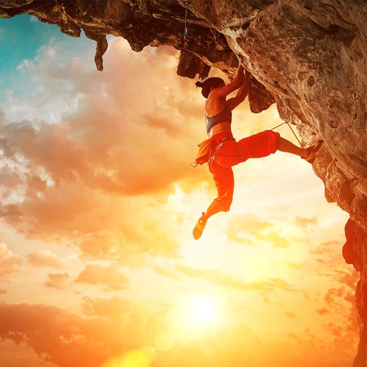Frau klettert an Klippe hoch bei Sonnenuntergang